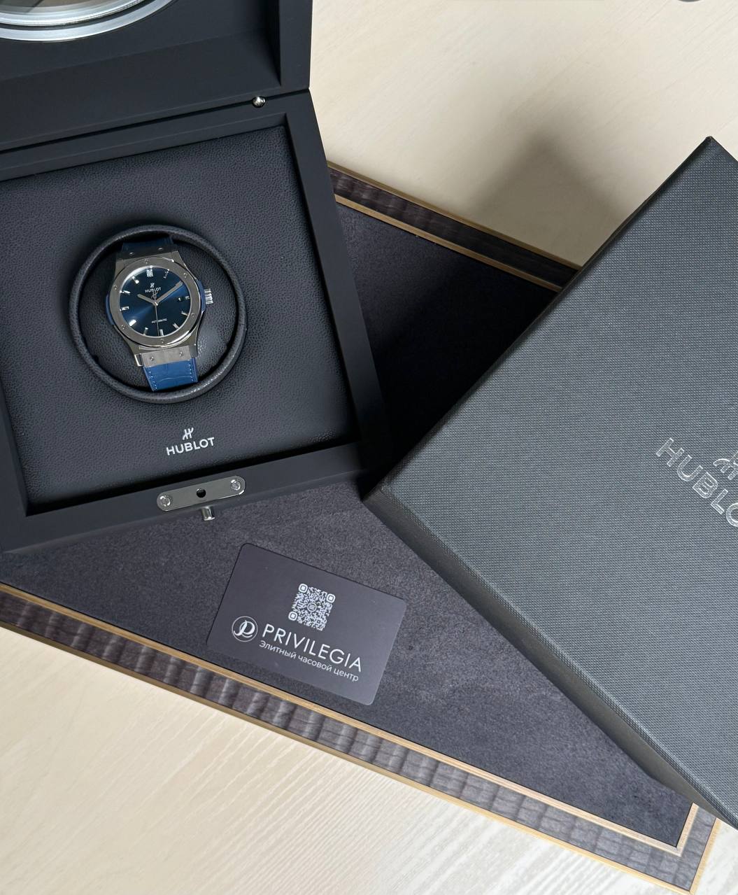 Hublot wristwatch with blue strap in a black presentation box, the box open on a textured surface with a Privilegia card nearby