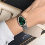 Women's luxury wristwatch with an emerald green dial, diamond-studded bezel, and a two-tone metal bracelet on a wrist.
