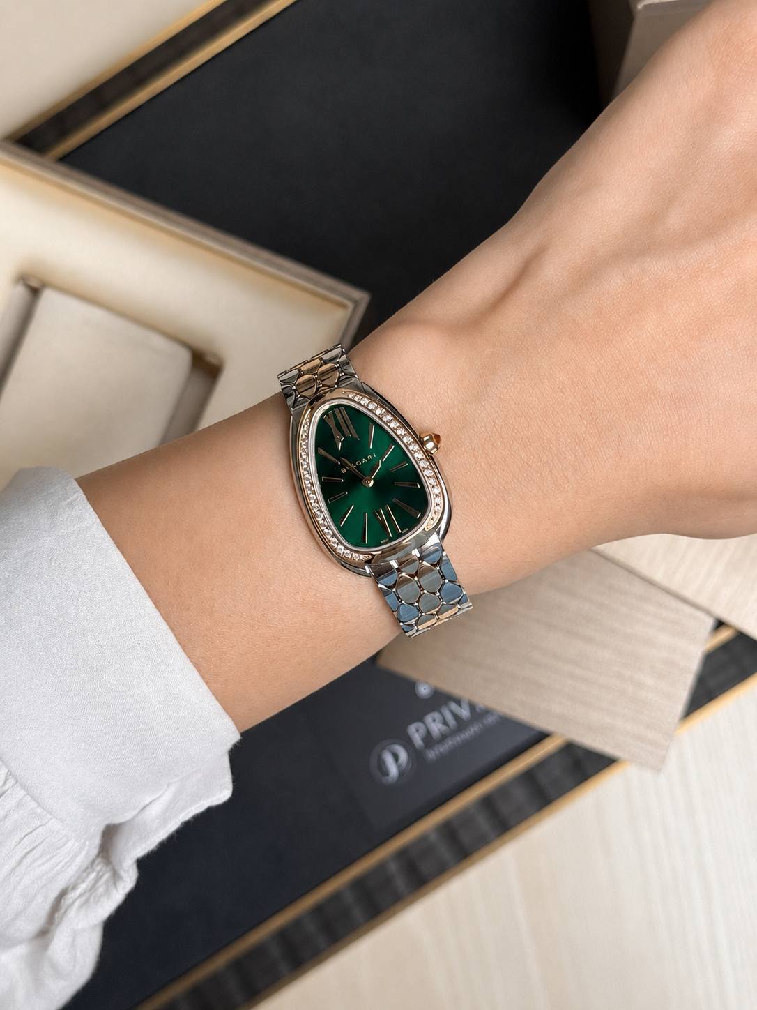 Women's luxury wristwatch with an emerald green dial, diamond-studded bezel, and a two-tone metal bracelet on a wrist.