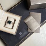 BVLGARI wristwatch in an open cream display box with a two-tone bracelet and a green dial, surrounded by brown textured packaging and cards.