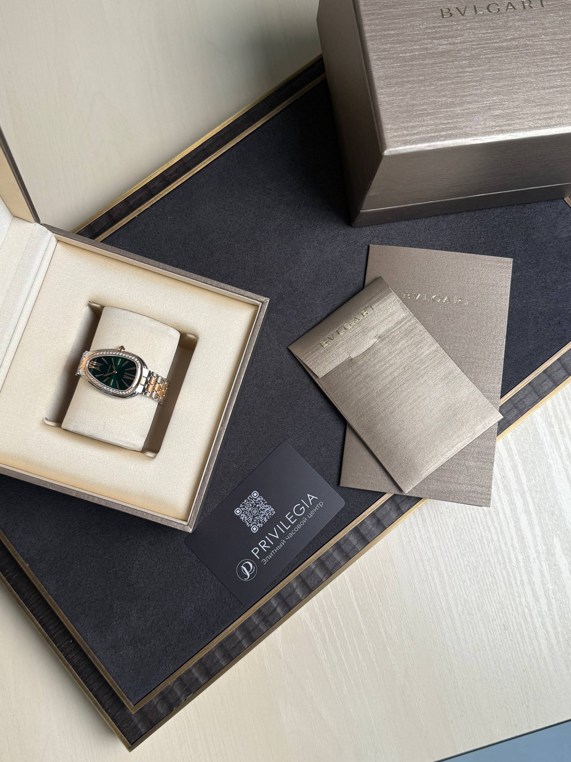 BVLGARI wristwatch in an open cream display box with a two-tone bracelet and a green dial, surrounded by brown textured packaging and cards.