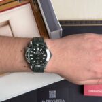 Wrist wearing a green Omega Seamaster dive watch with a black dial and luminous markers.