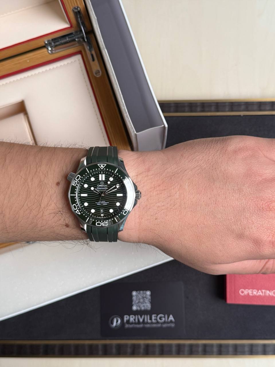 Wrist wearing a green Omega Seamaster dive watch with a black dial and luminous markers.