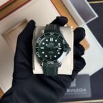 Green Omega Seamaster wristwatch on a cushioned display held by a gloved hand in a box.