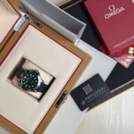 Omega wristwatch in a beige leather display box with a wooden frame and red interior lining, along with accompanying manuals and Privilege card nearby