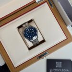 Omega dive watch with blue dial and silver bracelet in a beige, padded wooden presentation box.