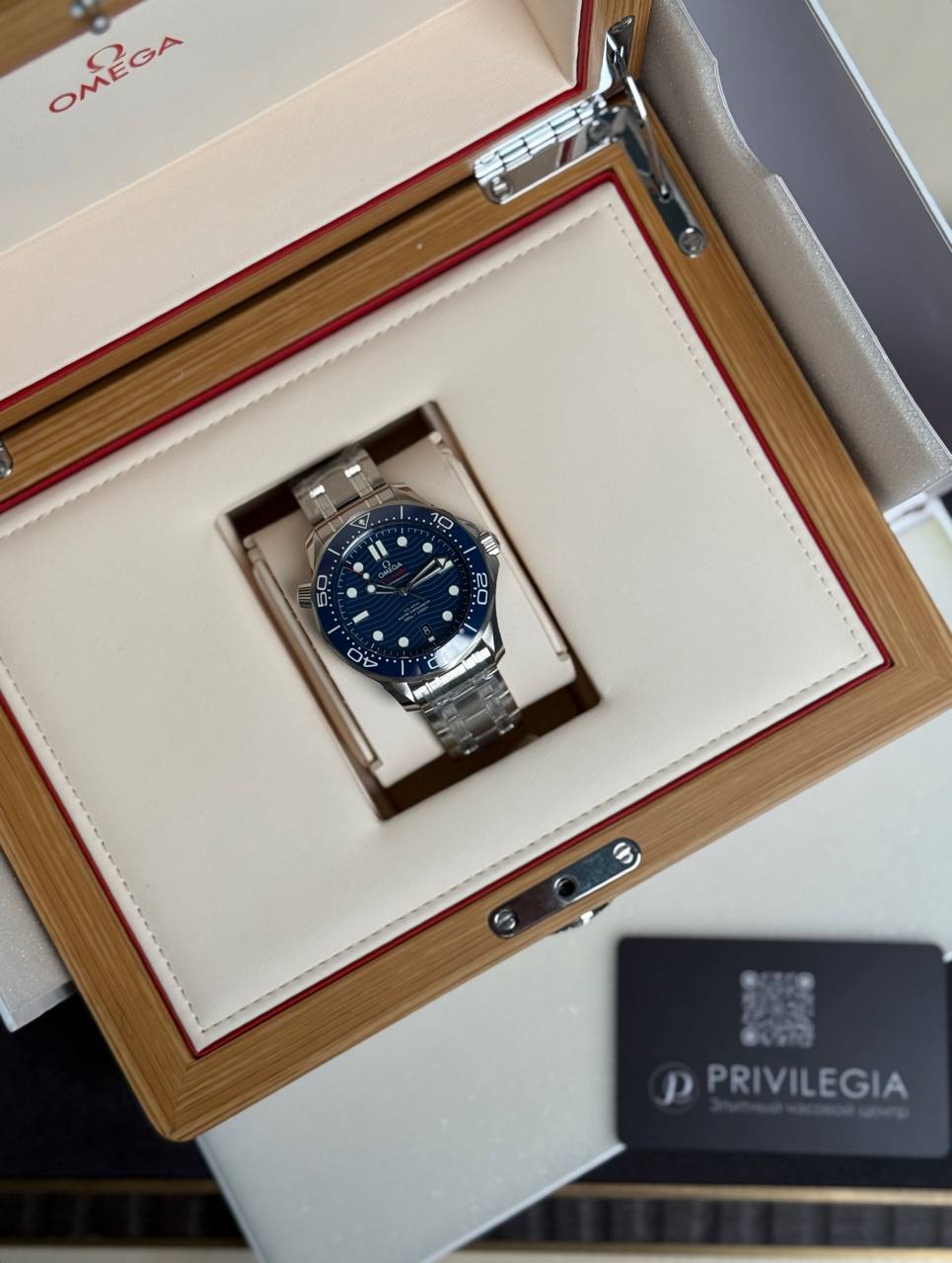 Omega dive watch with blue dial and silver bracelet in a beige, padded wooden presentation box.