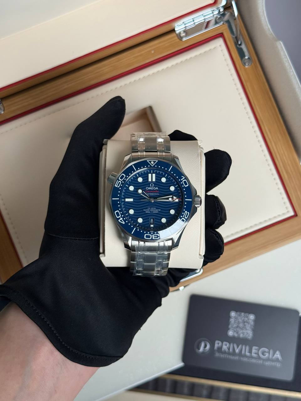 Omega dive watch with blue bezel and dial in a stainless-steel bracelet, held by a gloved hand over a white display cushion