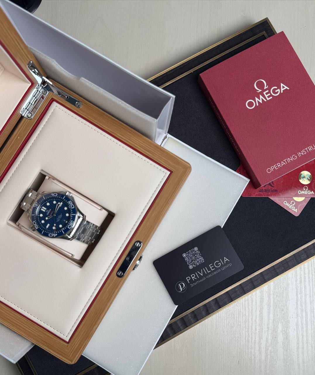 Omega wristwatch in a wooden presentation box with cream interior, blue dial, stainless steel bracelet, surrounded by manuals and cards