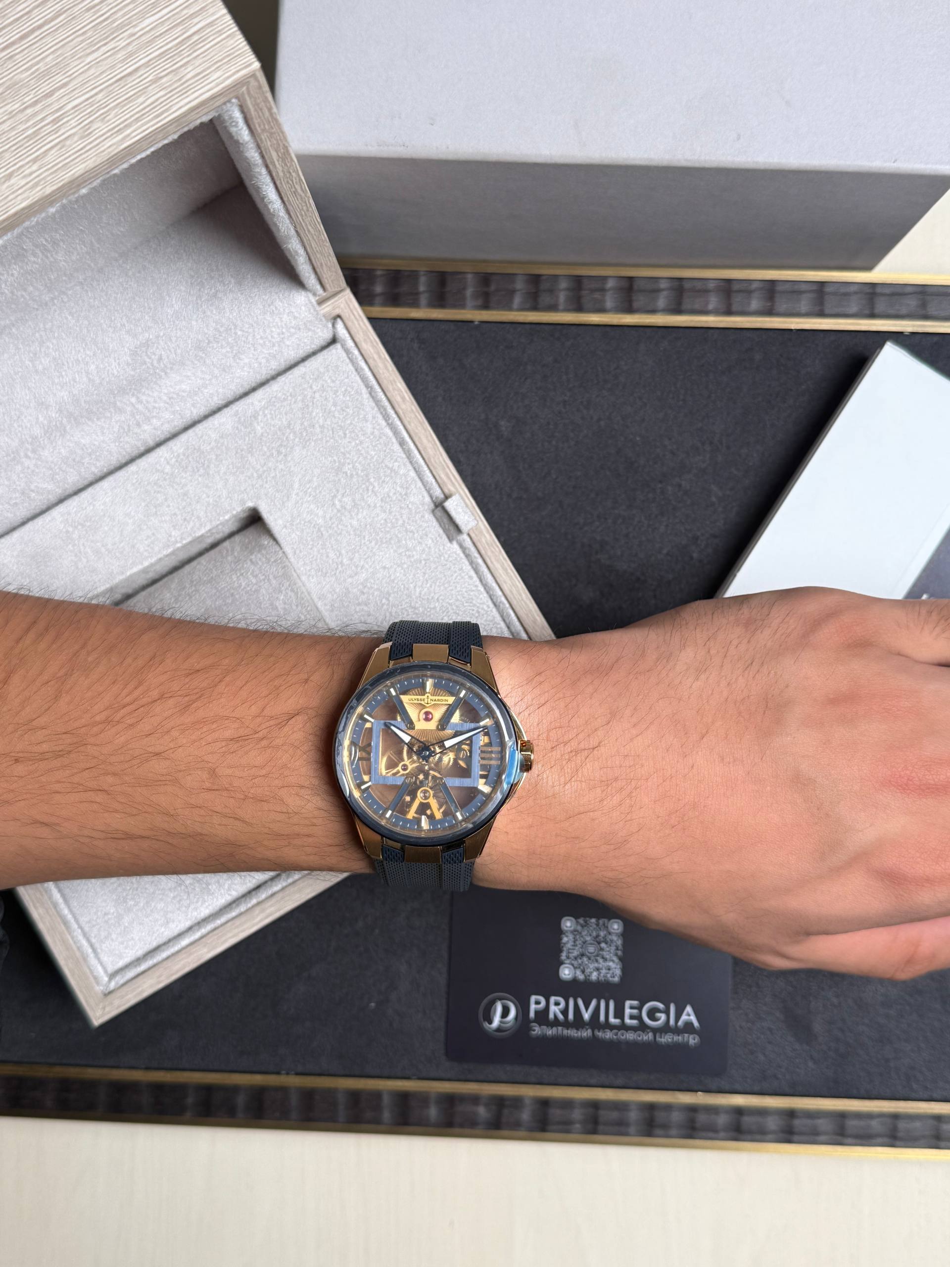 Wrist wearing a gold skeleton watch with a blue strap, resting next to an open jewelry box.
