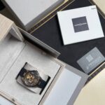 Luxurious wristwatch with a black strap displayed in an open gray box among other packaging and a Ulysse Nardin logo box in the background.