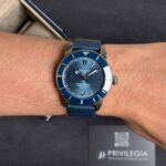 Blue Breitling Superocean wristwatch with blue bezel and strap on a wrist, with a dark display box in the background.