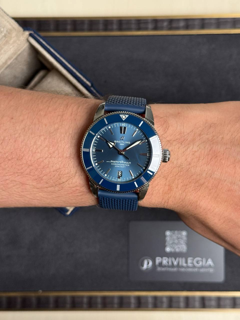 Blue Breitling Superocean wristwatch with blue bezel and strap on a wrist, with a dark display box in the background.