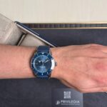 Blue Breitling wristwatch with a blue strap on a forearm, resting on a presentation box with a Privilegia card nearby.