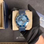 Blue Breitling Superocean watch on a beige display cushion, worn on a gloved hand, in a jewelry box.
