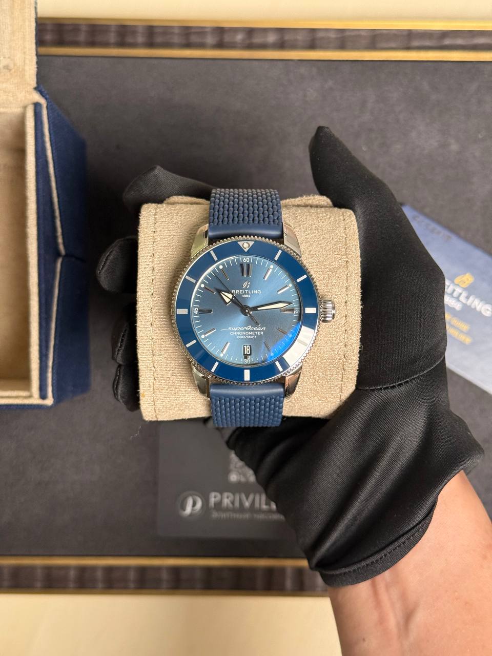 Blue Breitling Superocean watch on a beige display cushion, worn on a gloved hand, in a jewelry box.