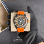 Orange-strapped Breitling watch held in gloved hand in a presentation box.