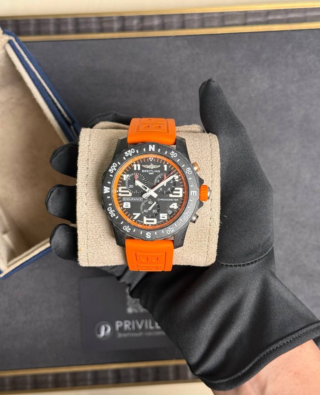 Orange-strapped Breitling watch held in gloved hand in a presentation box.