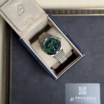 Silver wristwatch with a green dial in a beige padded display box inside a dark luxury presentation box with a Privilegia card nearby.