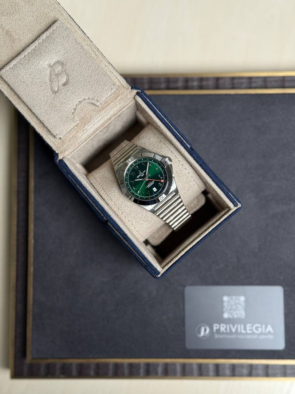 Silver wristwatch with a green dial in a beige padded display box inside a dark luxury presentation box with a Privilegia card nearby.
