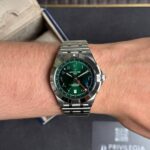 Breitling wristwatch with a green dial and metal bracelet worn on a forearm wrist.