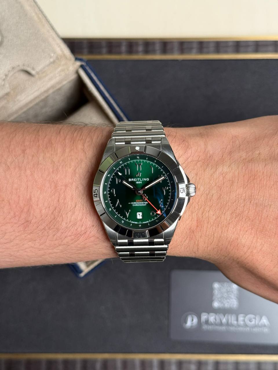 Breitling wristwatch with a green dial and metal bracelet worn on a forearm wrist.