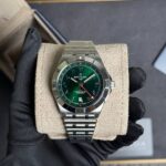 Breitling stainless steel wristwatch with green dial on a beige cushion, held by a gloved hand (dressy, luxury timepiece)