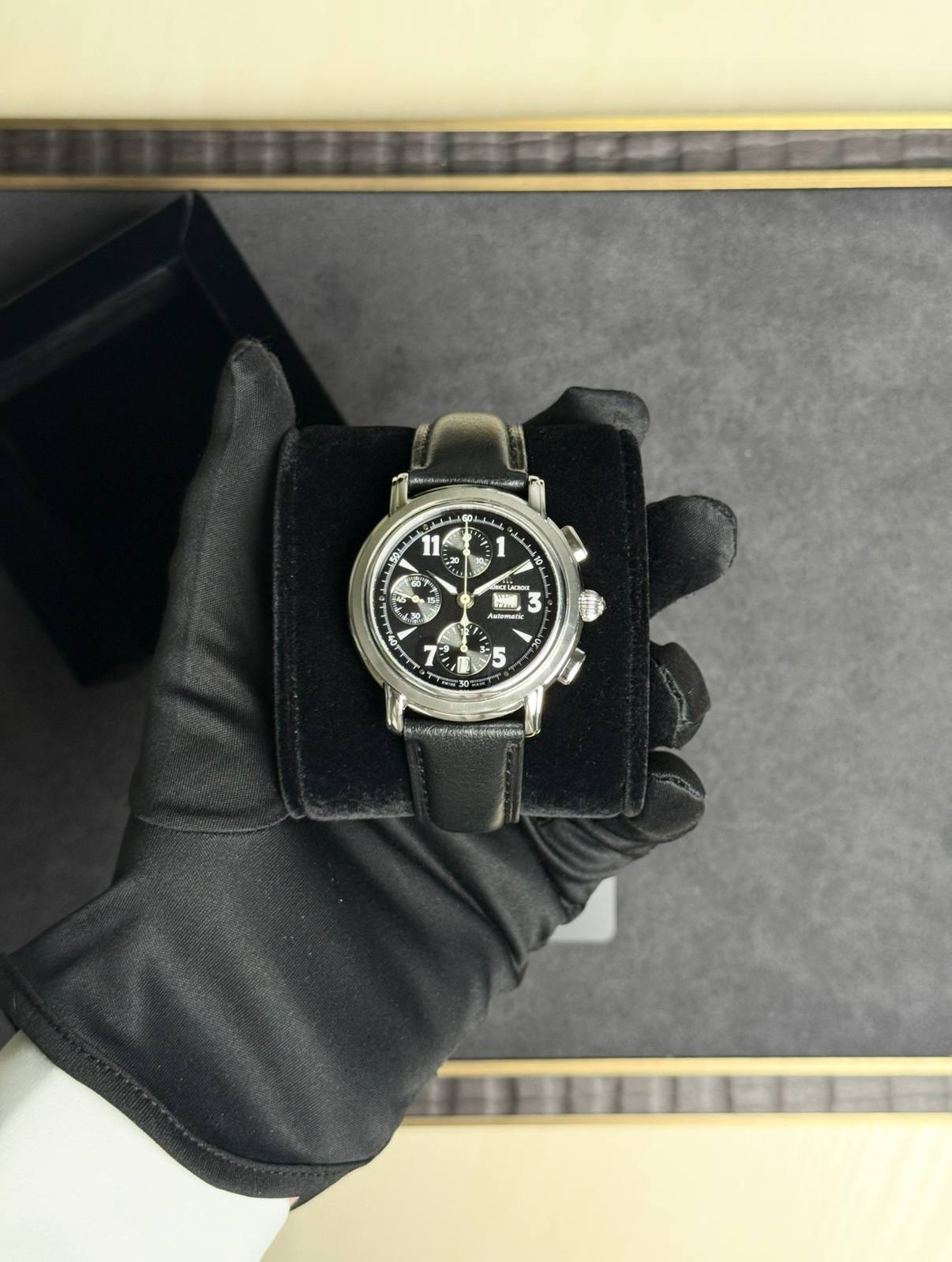 Chronograph wristwatch with black dial and leather strap held in a black presentation box