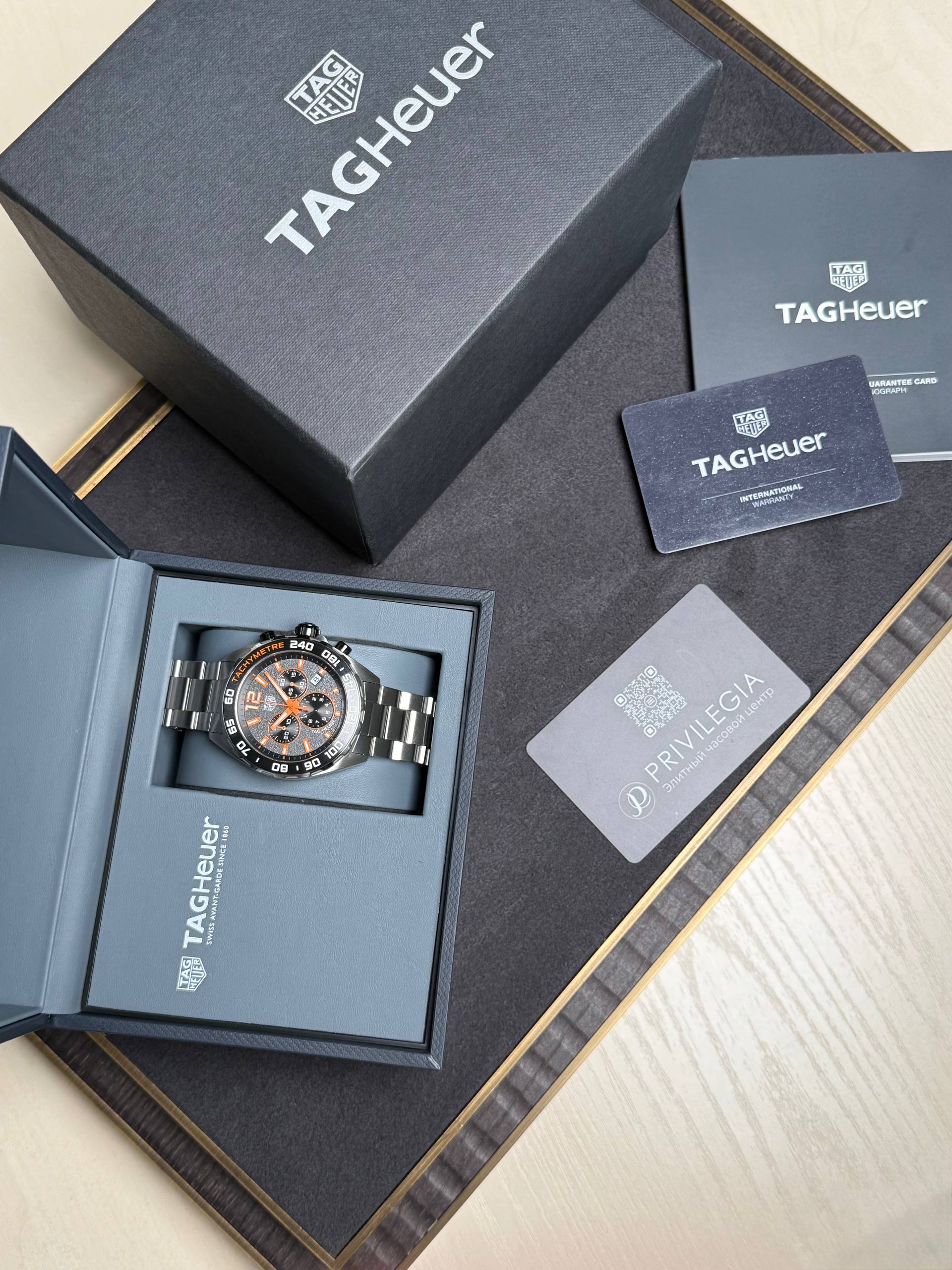 TAG Heuer watch in an open navy presentation box with accompanying guarantee card and booklet on a dark textured surface.