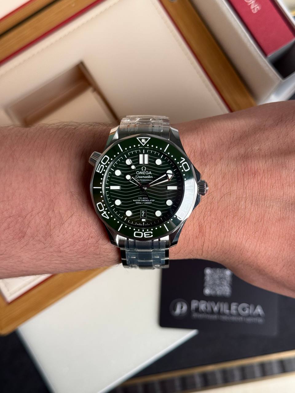 Wrist wearing a green-bezel Omega Seamaster diver's watch with a stainless steel bracelet.