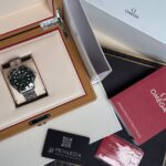 Omega stainless steel wristwatch in an open beige presentation box with red trimming, surrounded by Omega manuals and a Privilega card