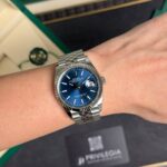 Silver Rolex Datejust wristwatch with a blue dial and magnified date window showing 31, worn on the left wrist.