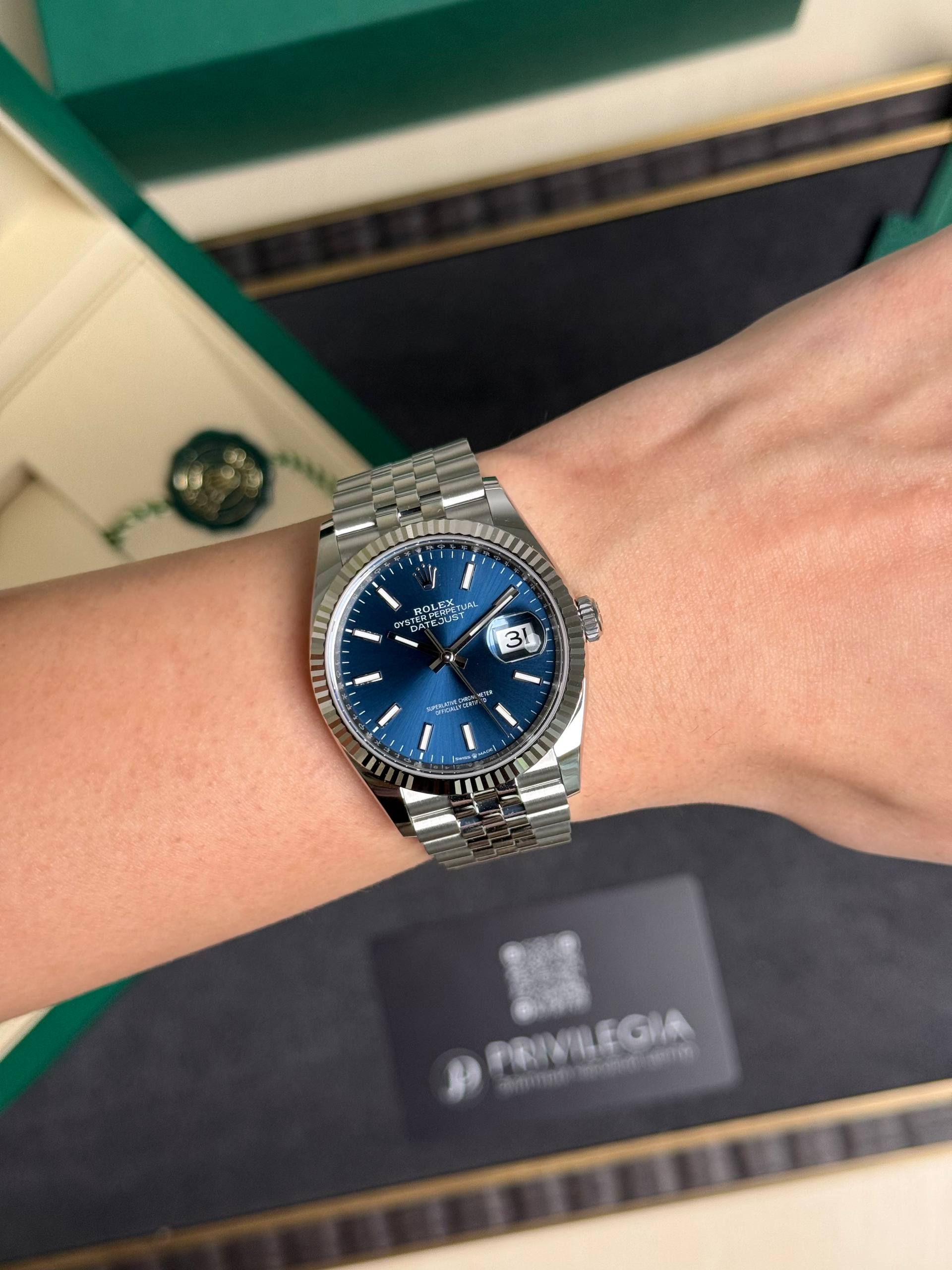 Silver Rolex Datejust wristwatch with a blue dial and magnified date window showing 31, worn on the left wrist.