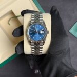 Rolex Datejust wristwatch with a blue dial and silver bracelet resting on a beige display cushion in a green Rolex box