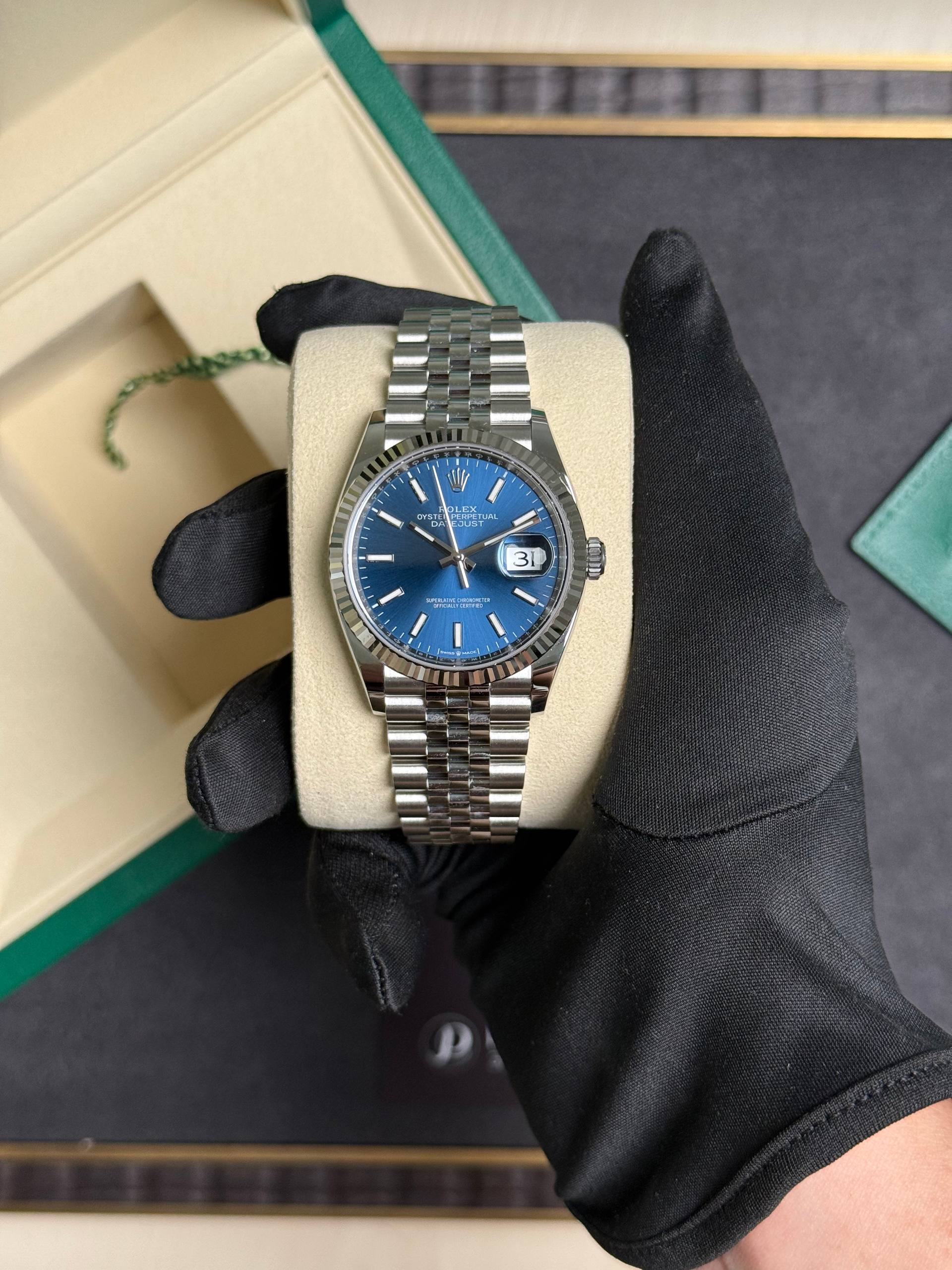 Rolex Datejust wristwatch with a blue dial and silver bracelet resting on a beige display cushion in a green Rolex box