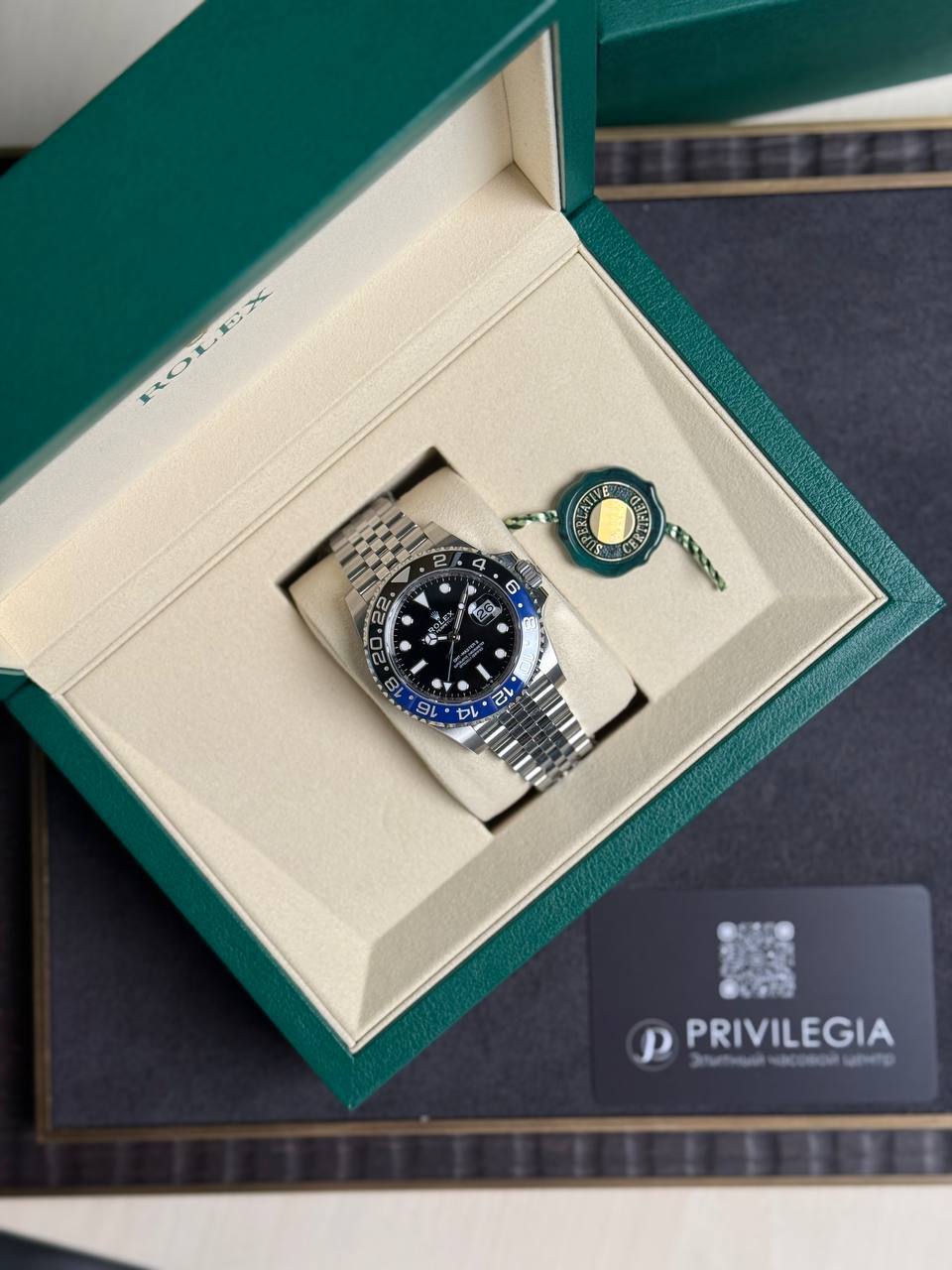 Rolex GMT-Master II watch with blue/black bezel in an open green presentation box with green seal tag nearby.