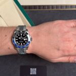 Wrist wearing a stainless steel Rolex GMT-Master II 'Batman' watch with blue and black bezel, resting on a dark presentation box with a Privilegia card nearby, indoors