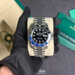 Rolex GMT-Master II with a blue and black bezel, black dial, and Jubilee bracelet held by a gloved hand on a display cushion.