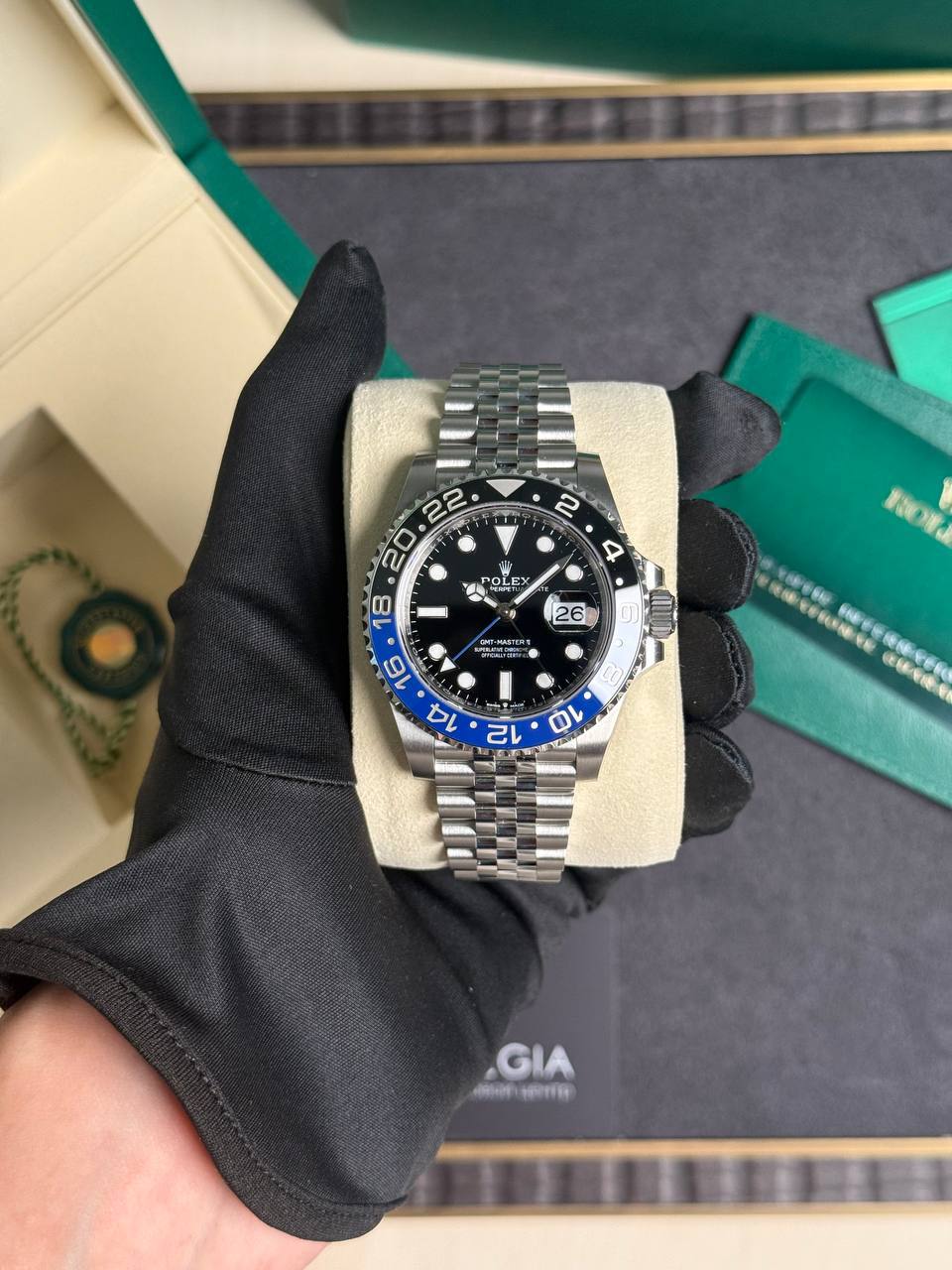 Rolex GMT-Master II with a blue and black bezel, black dial, and Jubilee bracelet held by a gloved hand on a display cushion.