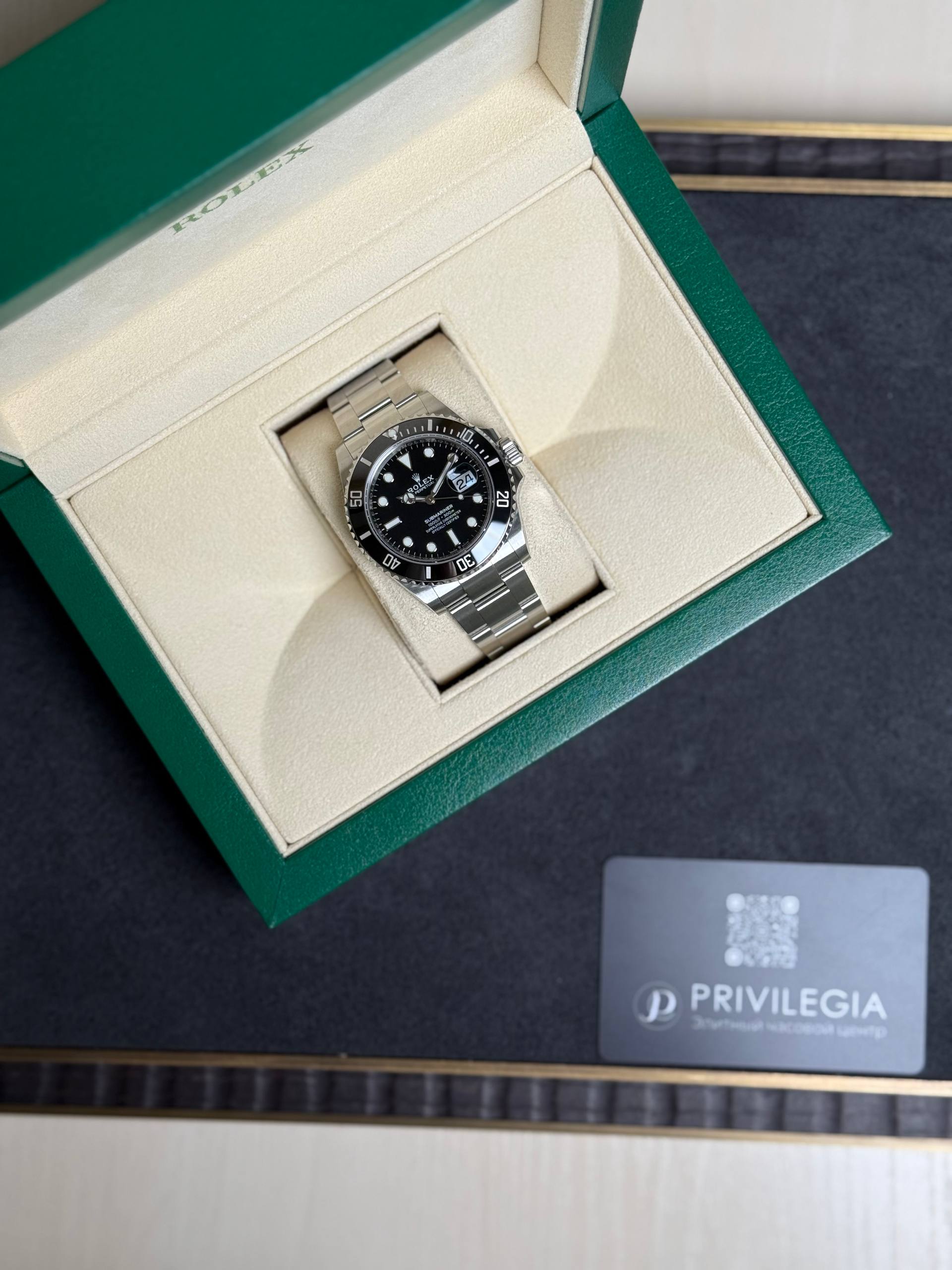 Rolex watch with black dial in a beige interior inside a green presentation box, metal bracelet visible.
