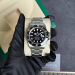 Stainless steel Rolex Submariner with black dial and date window, held by gloved hands in a beige display box.