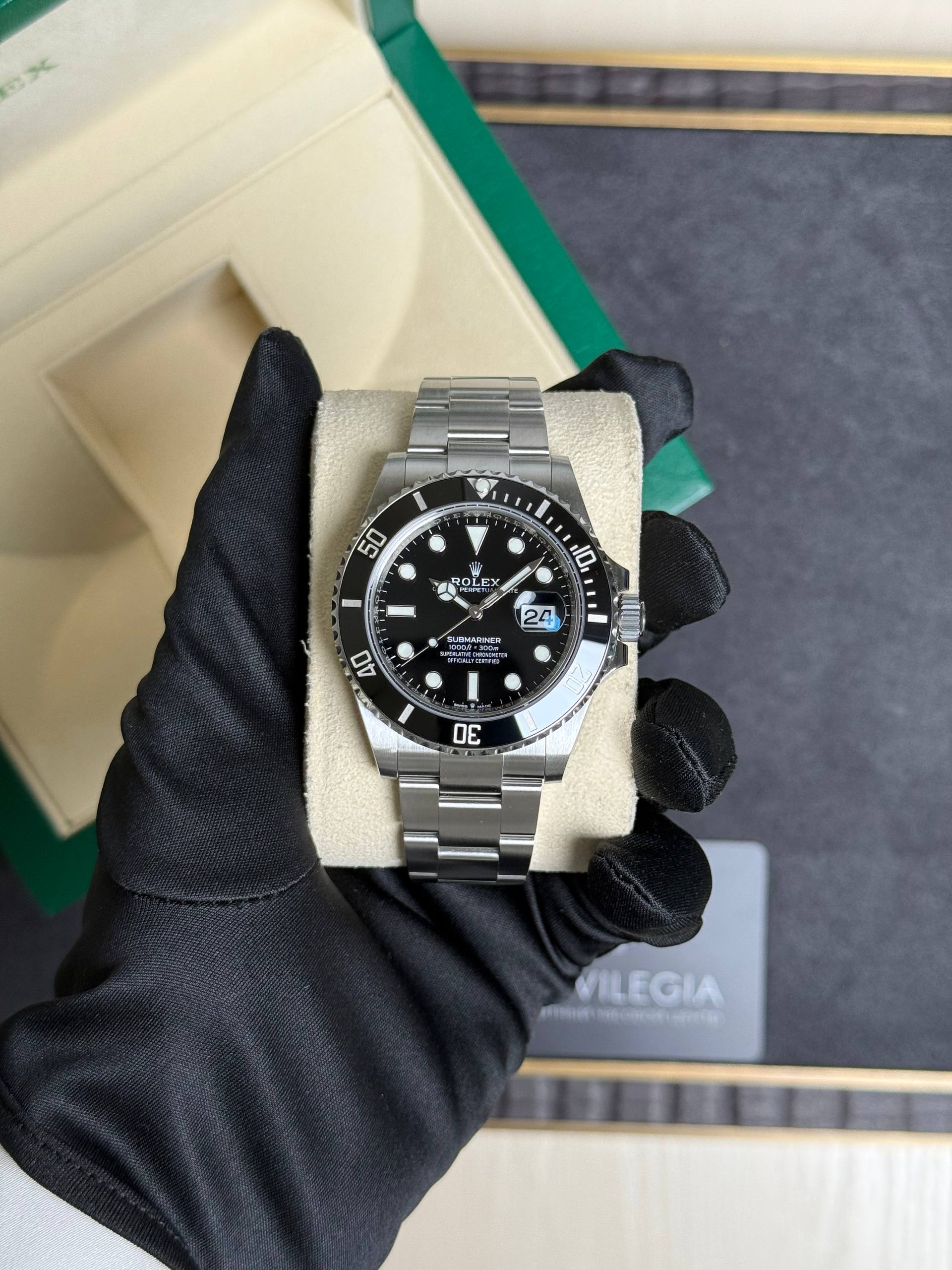 Stainless steel Rolex Submariner with black dial and date window, held by gloved hands in a beige display box.