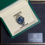 Rolex watch with blue dial in an open green presentation box.
