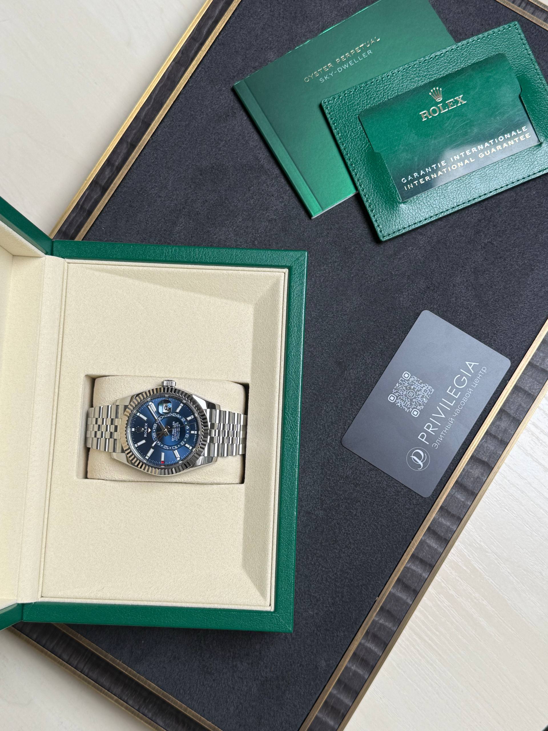 Rolex wristwatch in beige display box with green outer case and accompanying cards on a dark surface.