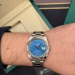 Wrist wearing a stainless steel Rolex Datejust with a blue dial, Roman numeral hour markers, and a date window at 3 o'clock.