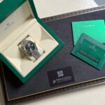 Rolex wristwatch in an open green box on a desk, with green manuals and a Privilegia card nearby.