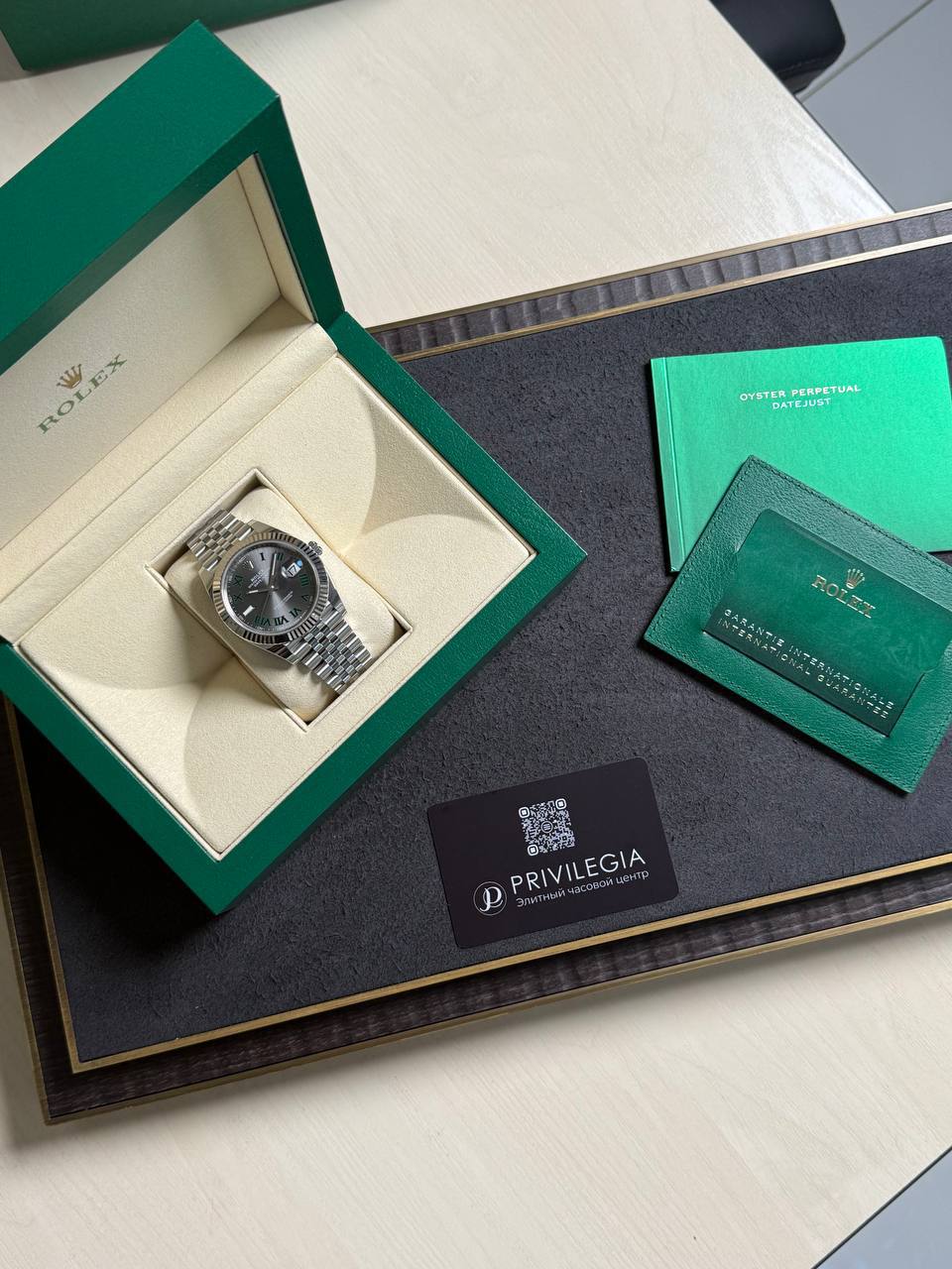 Rolex wristwatch in an open green box on a desk, with green manuals and a Privilegia card nearby.