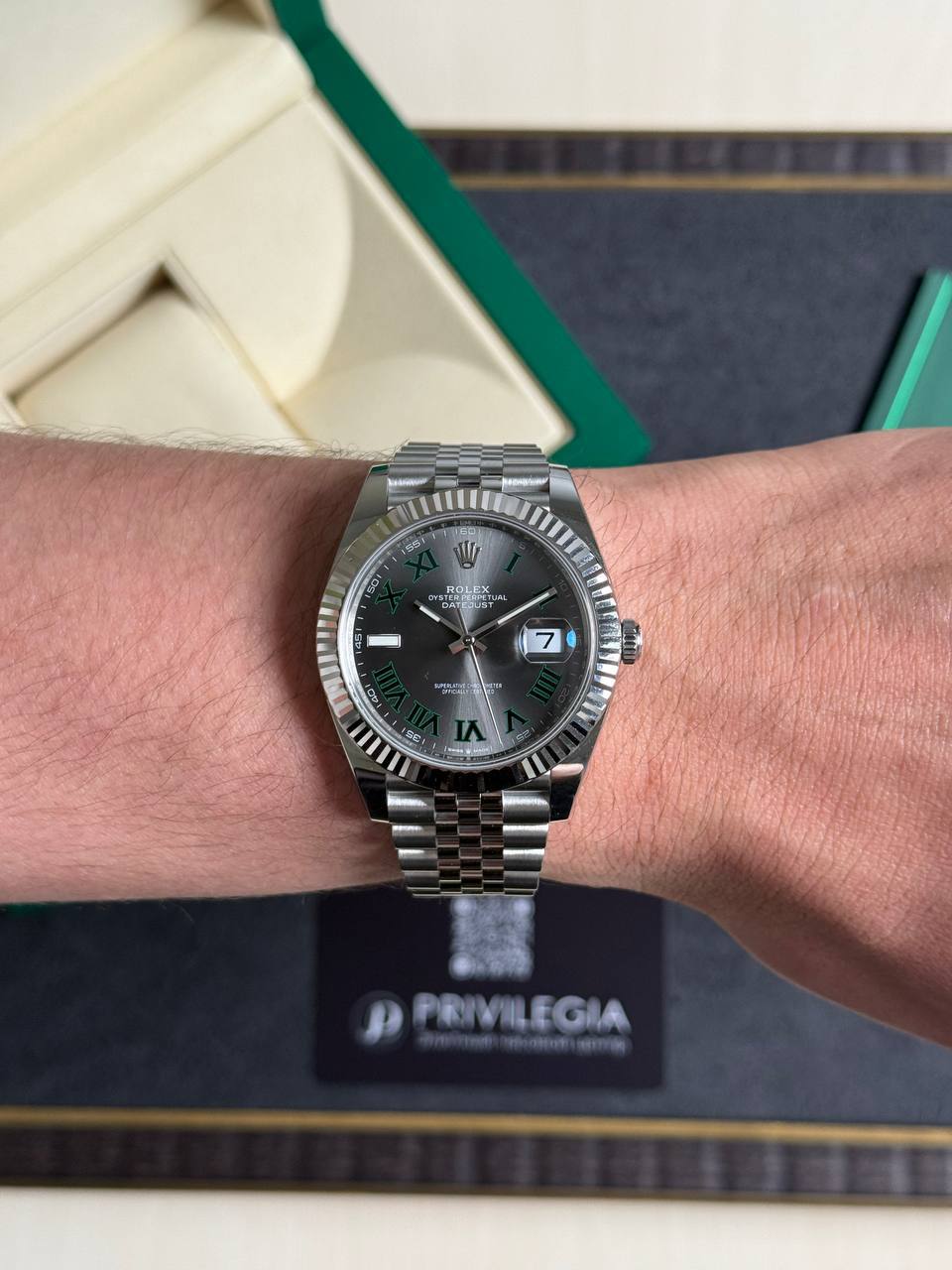 Stainless steel Rolex Datejust on a wrist, with green Roman numeral markers and a date window at 3 o'clock.