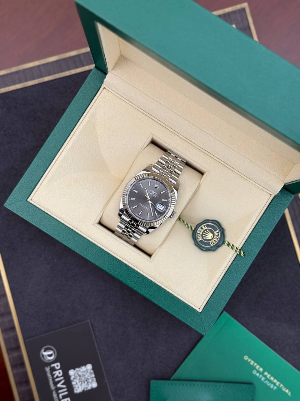 Rolex Oyster Perpetual Datejust in a green presentation box with cream interior and a hanging Rolex tag