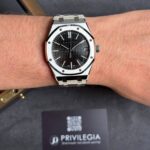 A stainless steel Audemars Piguet Royal Oak wristwatch with a black textured dial and date window on the wrist.